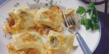 4 Maultaschen mit geschmorten Zwiebeln auf einem Teller, dazu Petersilie