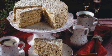 angeschnittene Torte auf Porzellan-Etagere, daneben edles Kaffeservis und ein Stück  auf einem Teller