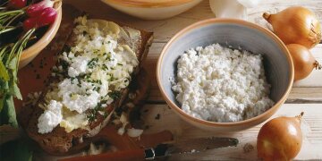 hölzerne Tischplatte mit einem Brot mit Ziebeleskäs, daneben eine Schüssel mit Ziebeleskäs, Zwiebeln, Radieschen, ein Messer
