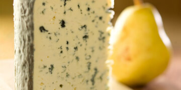 ein Stück Edelpilzkäse, Nahaufnahme, im Hintergrund eine Birne