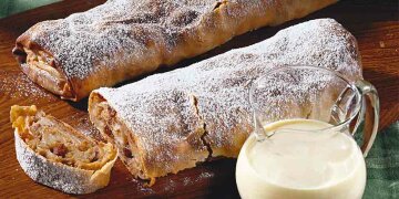 2 Strudel auf Holztisch, einer angeschnitten, daneben ein Krug Milch