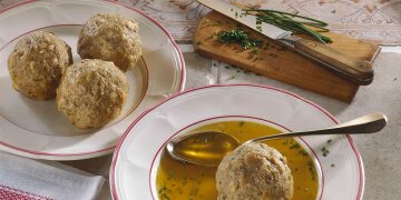 Suppenteller mit Brühe, darin ein Leberknödel, daneben ein silberner Löffel
