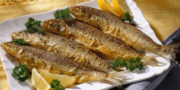 4 zubereitete Renken auf einer Servierplatte, neben Zitrone und Petersilie