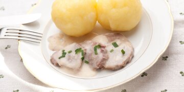 Drei Scheiben Fleisch mit Meerettichsoße, dazu zwei Klöße, angerichtet auf einem weißen Teller