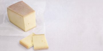 ein großes Stück Sennalpkäse auf Wachspapier, 2 Scheiben davor