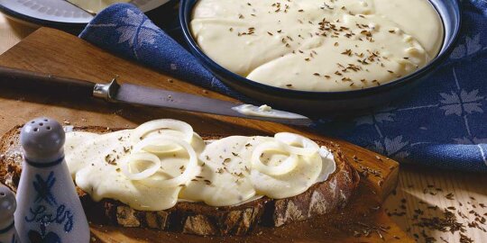 ein Brot mit Kochkäs beschmiert, ein Streichmesser, einer Form mit Kochkäs, daneben ein Salzstreuer