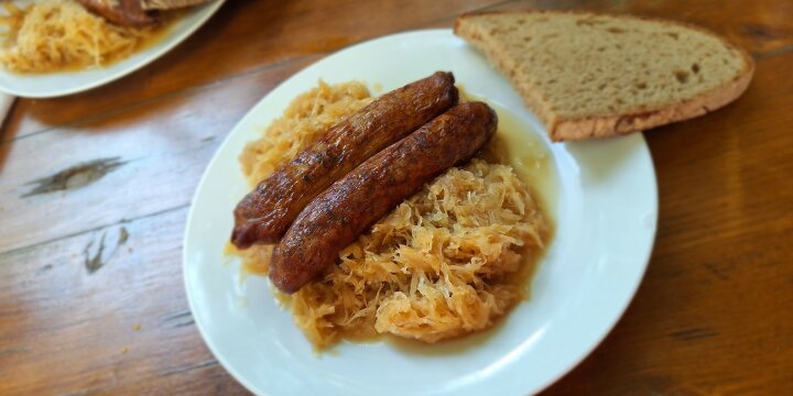 Zwei Treuchtlinger Bratwürste mit Sauerkraut, angerichtet auf einem weißen Teller, daneben eine Scheibe Brot