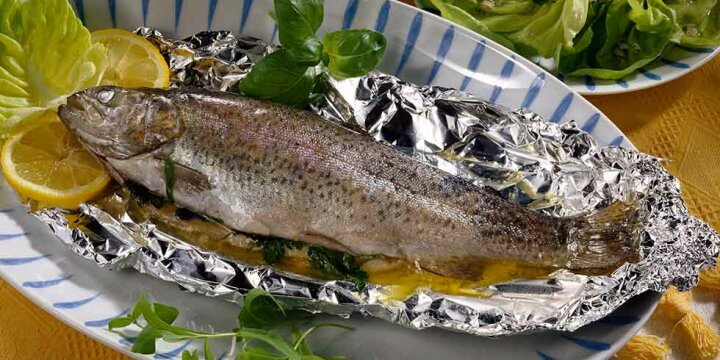 gegarte Forelle auf Fischplatte, aufgepackte Alufolie, mit Zitrone, Salat garniert